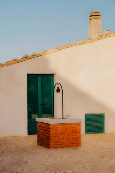 A house in Sicily with green doors and a red brick well