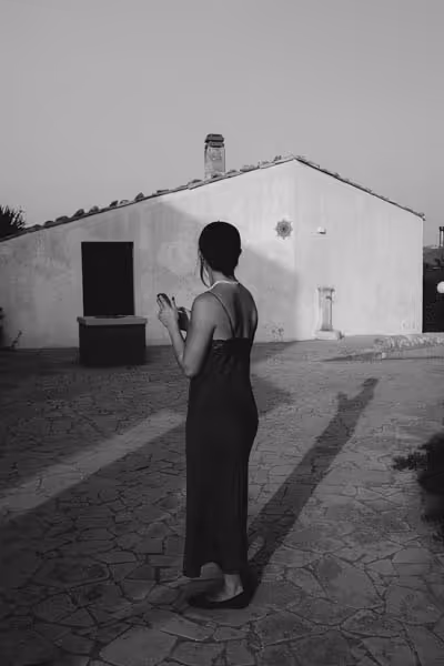 A woman in a dress with her back towards the camera looking at another house at sunset