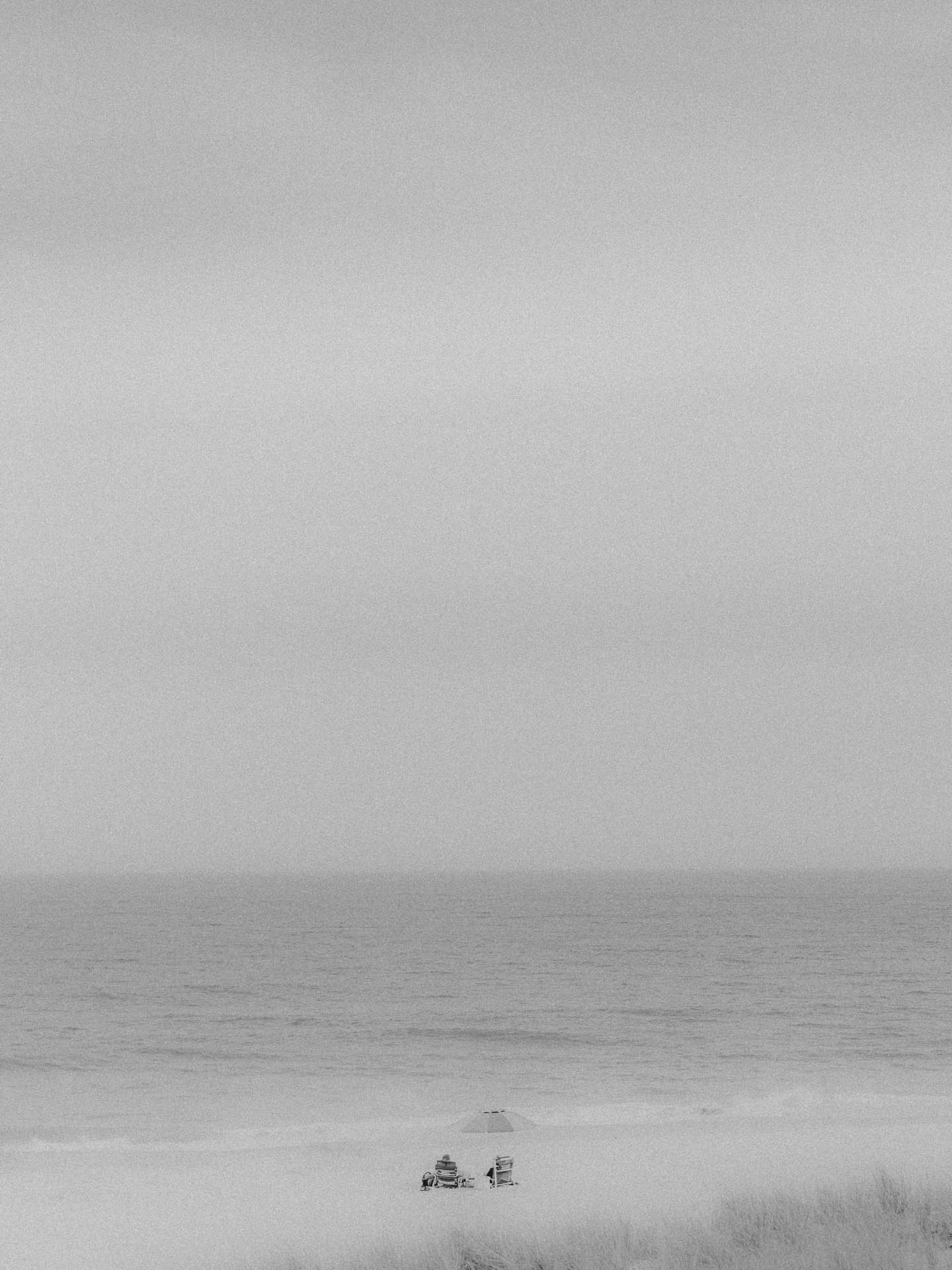 A couple at the beach on a rainy day with an umbrella in black and white