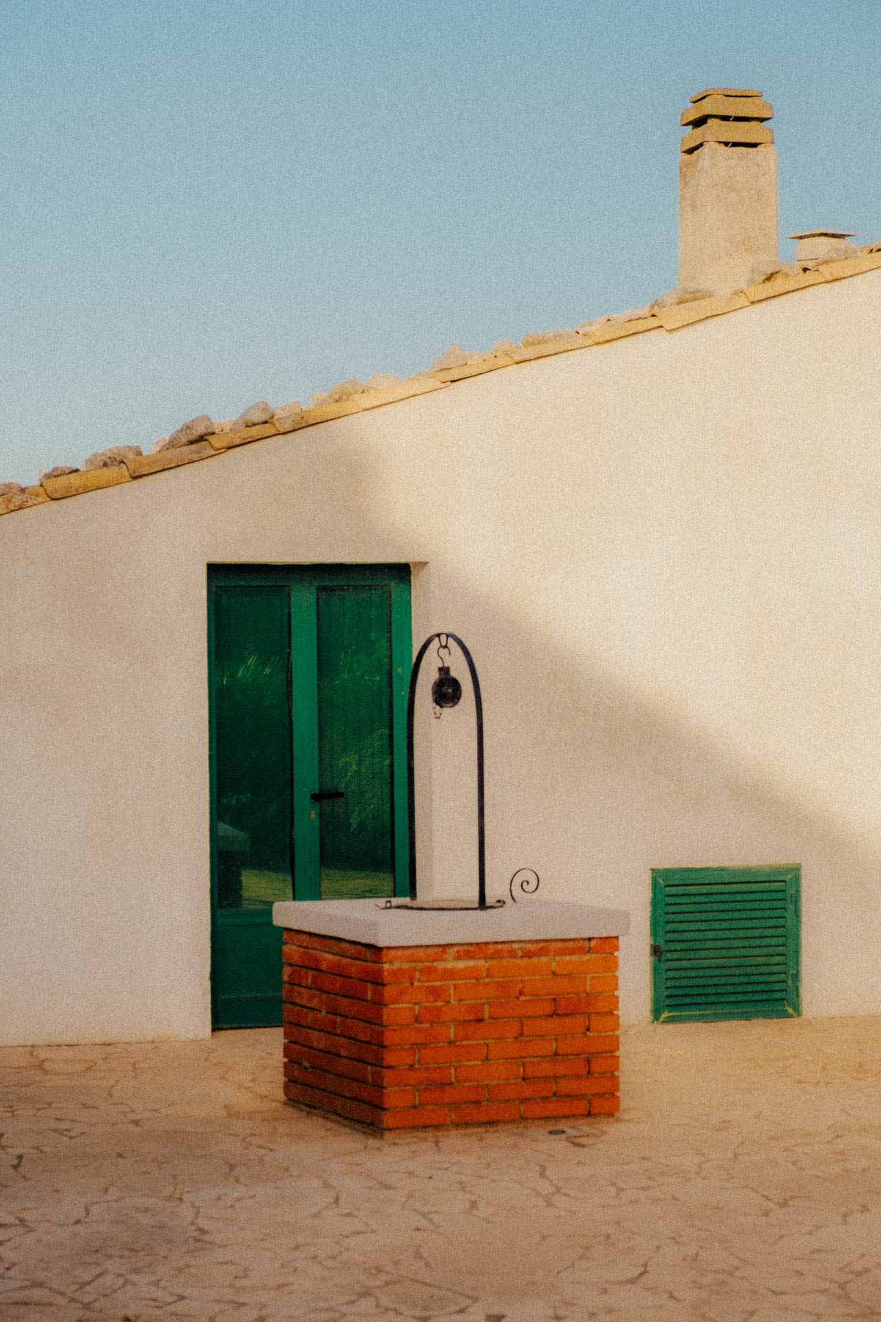 A house in Sicily with green doors and a red brick well