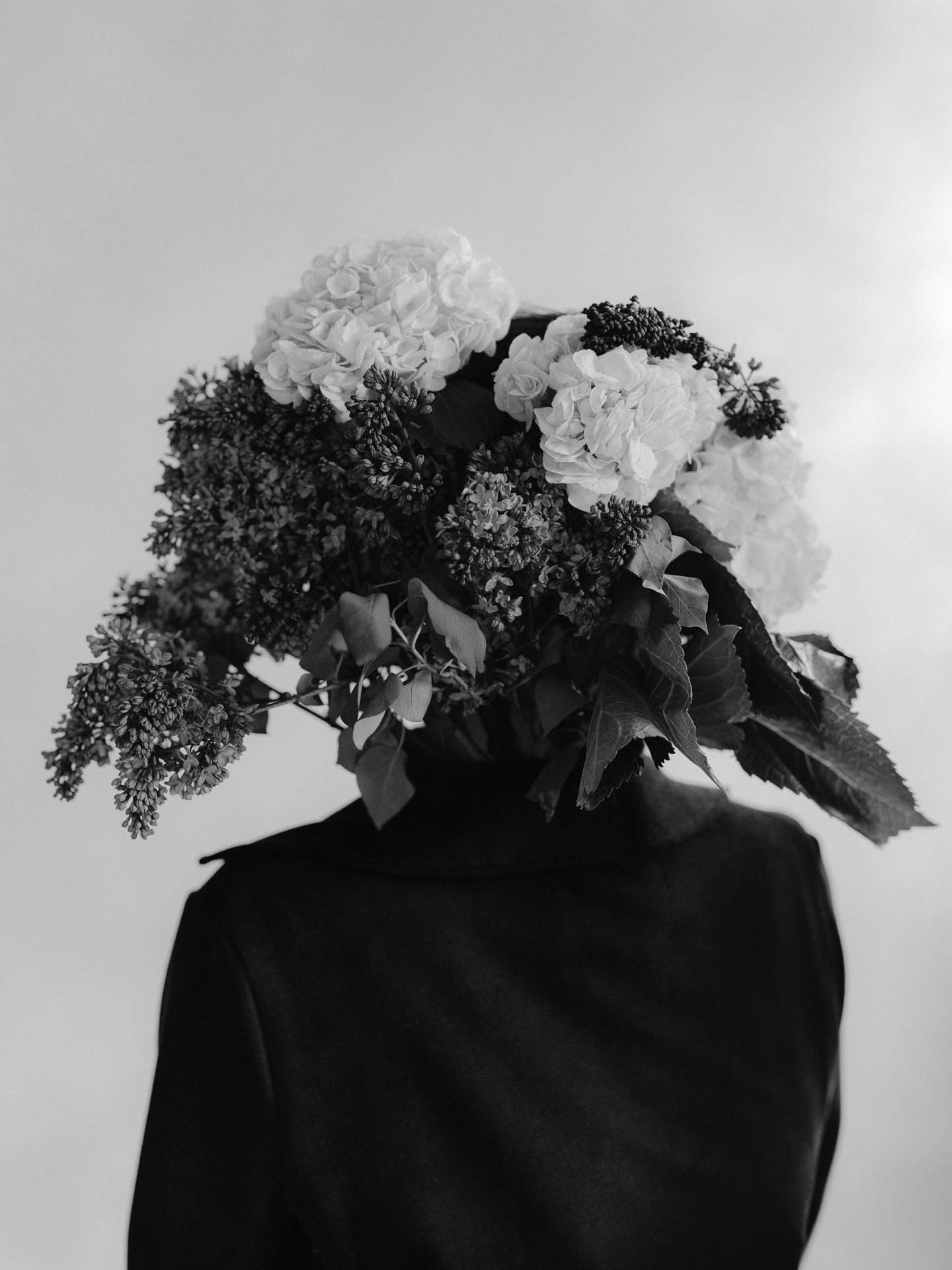 person with lilacs and hydrangea flower bouquet for a head. turtleneck and jacket in black and white