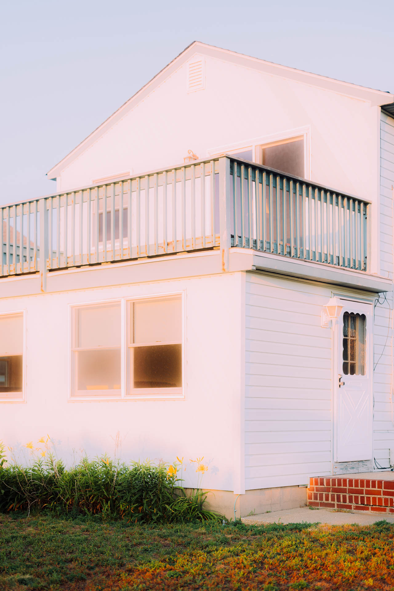 A glowing house in sunset with yellow flowers by the ocean