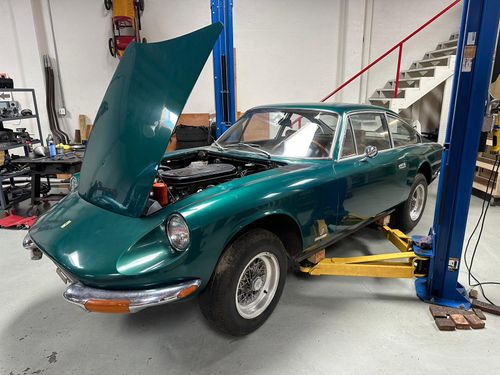 Vintage green Ferrari sports car undergoing maintenance on a hydraulic lift with its hood open in a garage workshop.