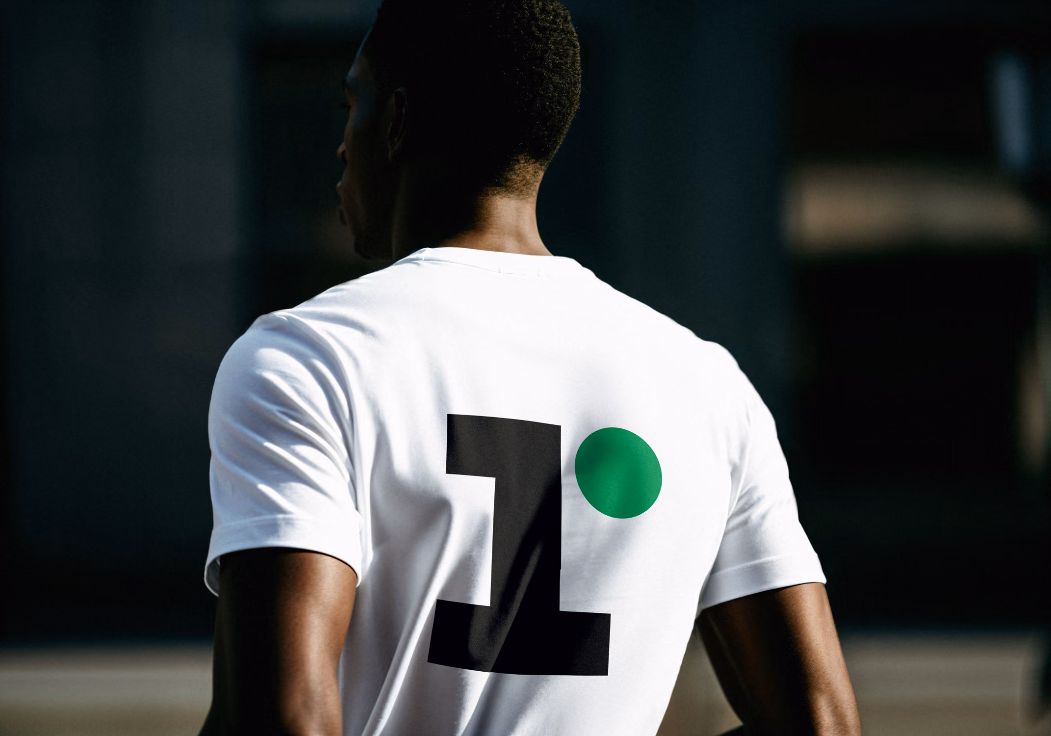 Rückansicht eines Mannes, der ein weißes T-Shirt mit großer schwarzer Zahl 1 und grünem Punkt trägt.