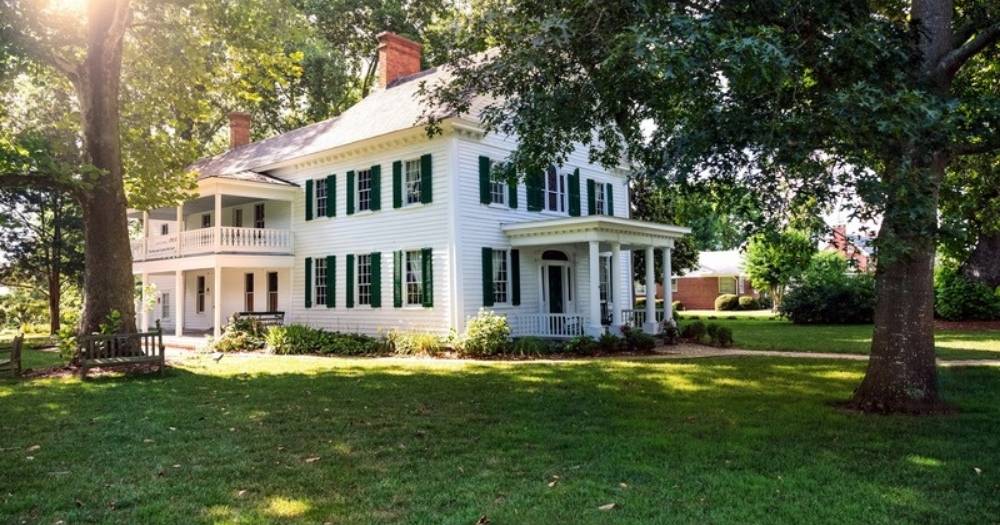 White two-story colonial home with green shutters under mature shade trees