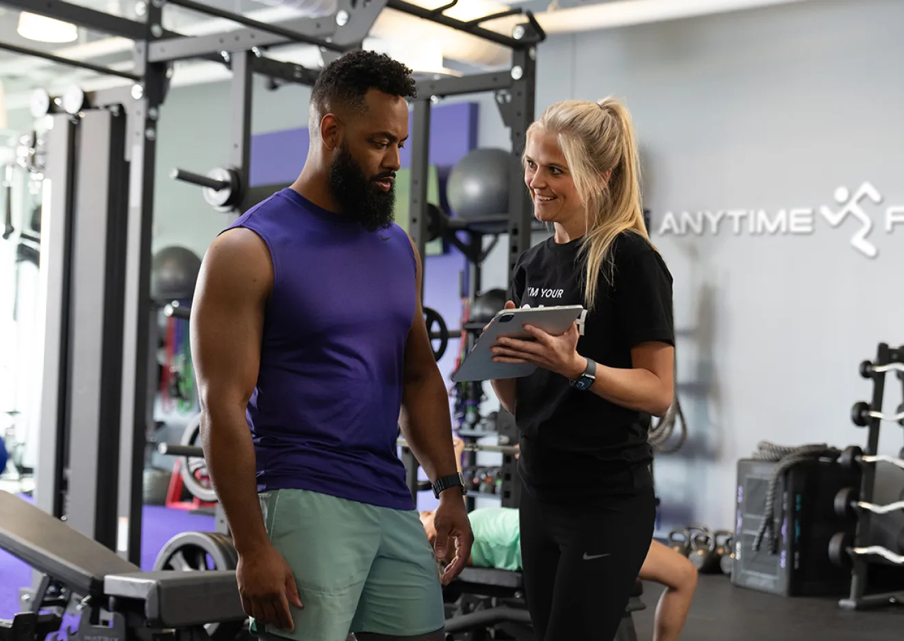 A personal trainer with a clipboard talking to a man in a gym.
