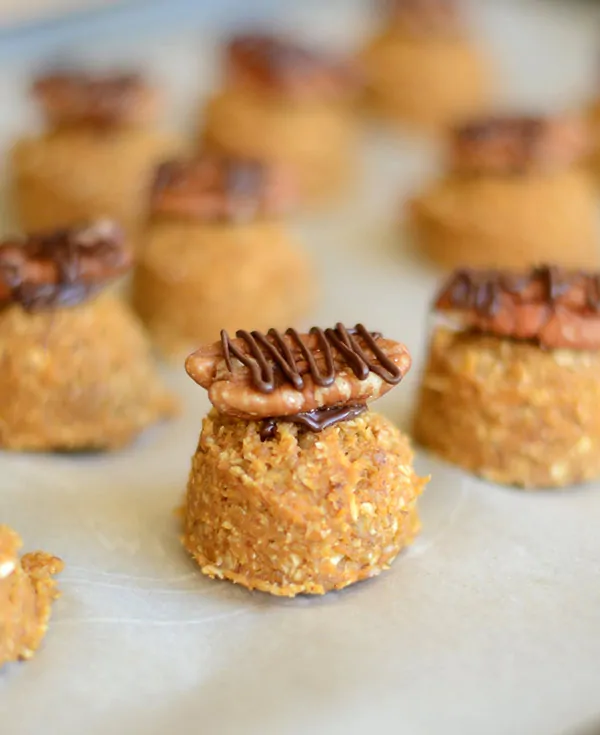 A close-up of homemade nut clusters topped with pecans and drizzled with chocolate, arranged on parchment paper.