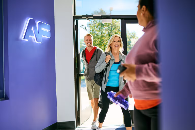 Group of gym members entering an Anytime Fitness club with a welcoming neon sign