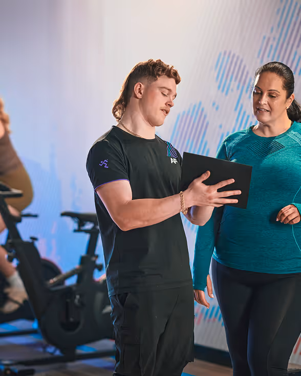 Trainer showing a workout plan on a tablet to a woman at the gym.