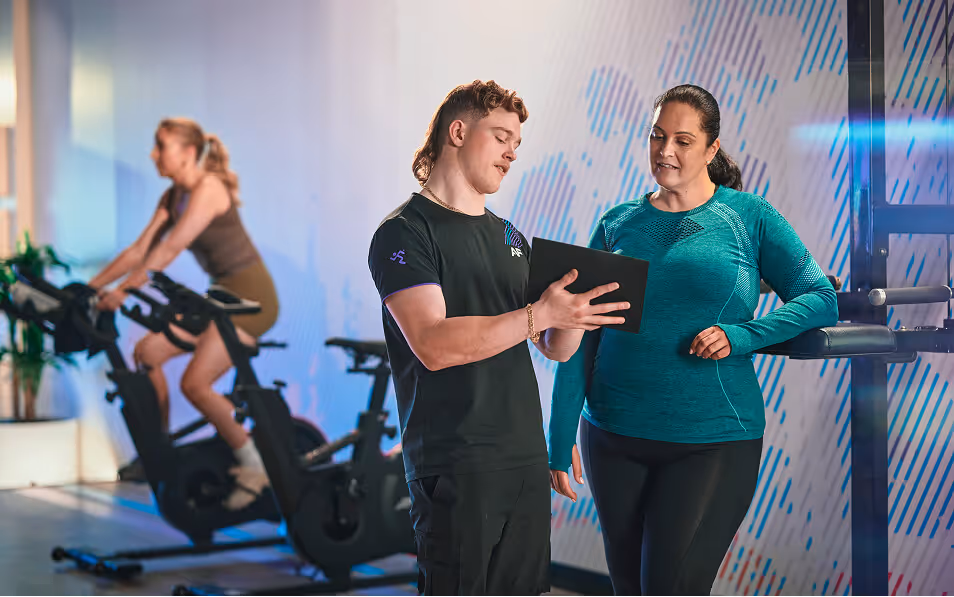 Focused woman performing cable fly exercise with a trainer in the background offering support.