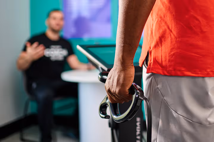 A person in a red shirt holds a fitness device while engaged in conversation with another individual seated at a table.