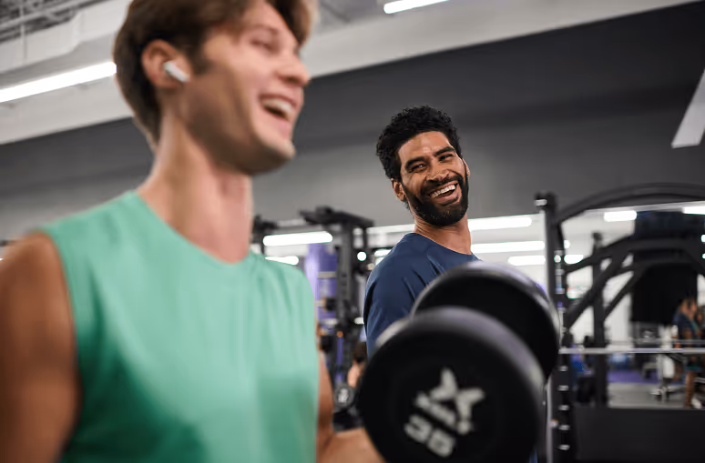Two men laughing and encouraging each other during a dumbbell workout at an Anytime Fitness gym.