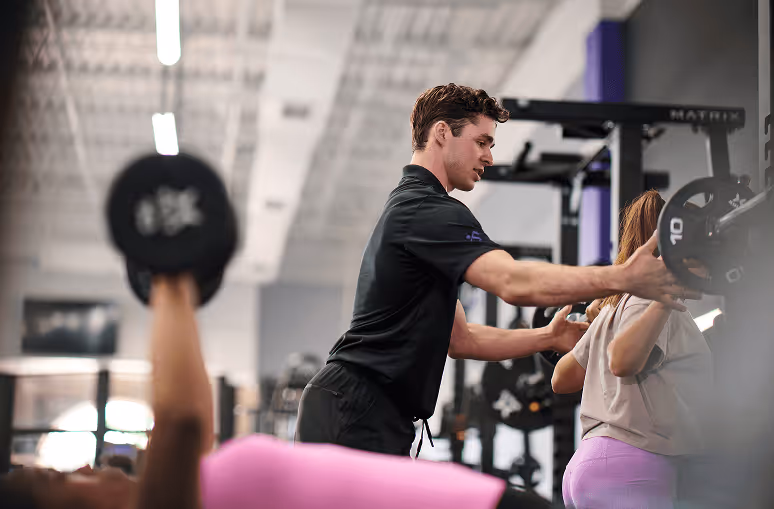 Anytime Fitness personal trainer providing a supportive spot for a member performing barbell squats.