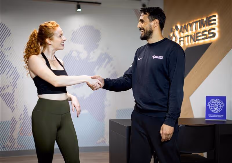 An Anytime Fitness coach welcoming a new member with a handshake, showcasing a friendly and supportive gym environment.