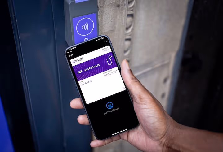 A person holding a smartphone showing an Anytime Fitness digital access pass near a contactless gym entry reader.