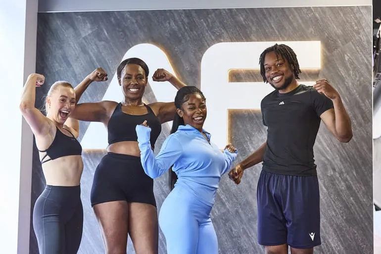 A group of four individuals flexing their muscles in fitness attire, standing in front of a stylish gym backdrop.