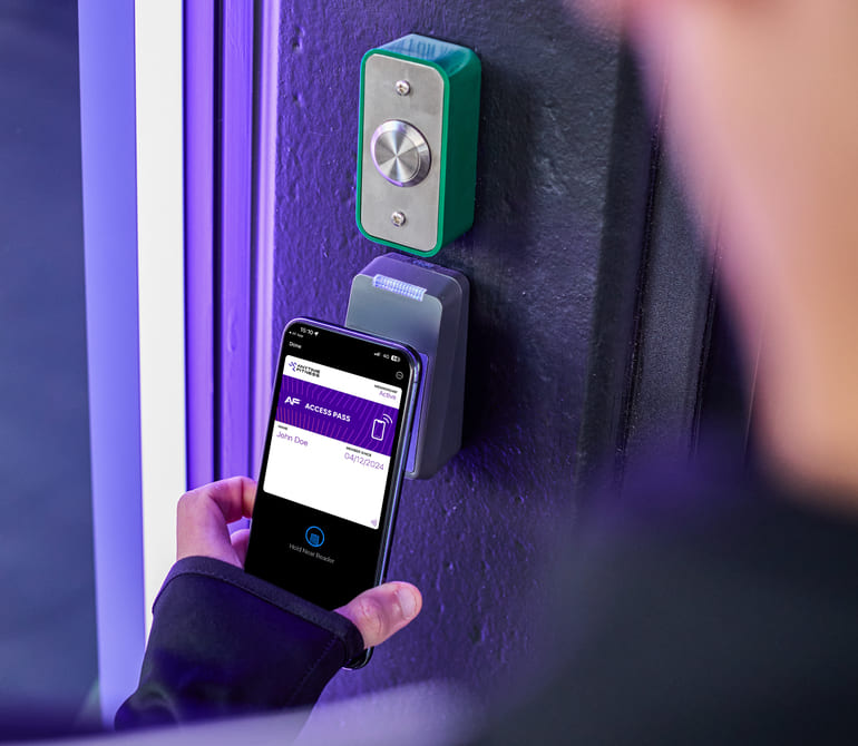 A person holds a smartphone near a digital access reader, displaying mobile credentials against a modern entry system.