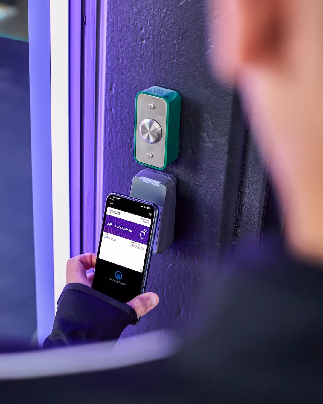 A person using the Anytime Fitness app on their smartphone to unlock a gym door via a contactless reader.