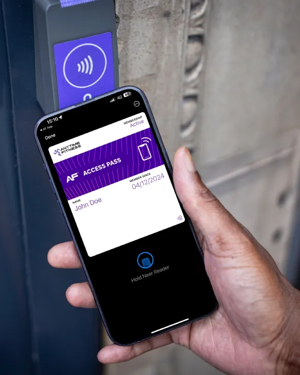 Hand holding a smartphone displaying an Anytime Fitness digital access pass near a contactless reader for entry.