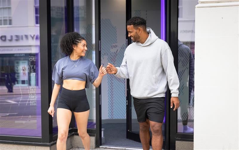 Two people outdoors fist bumping each other, one wearing a cropped t-shirt and the other a light gray hoodie.