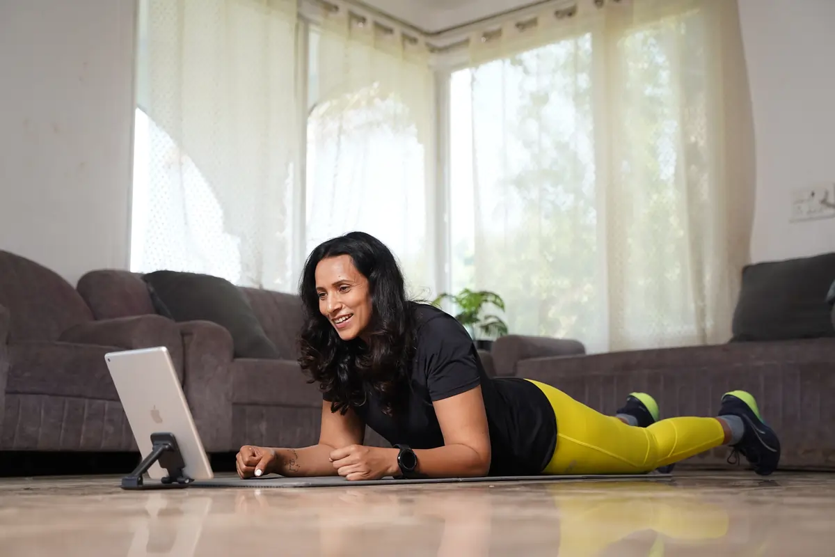 A woman follows a workout on a tablet while exercising at home, highlighting Anytime Fitness app support for guided workouts anytime, anywhere.