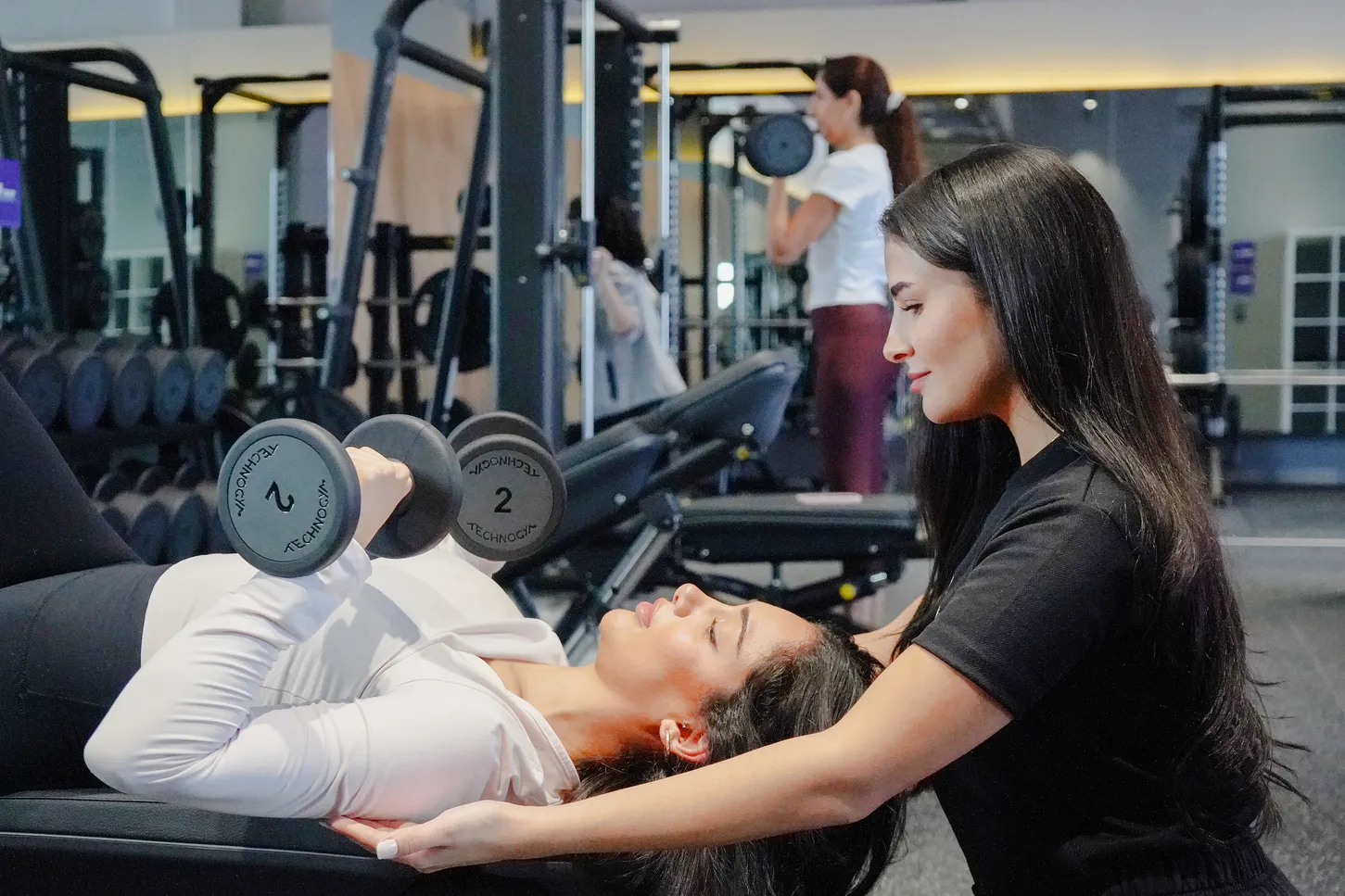 امرأة تؤدي تمرين سحب دمبل بيد واحدة على مقعد في صالة Anytime Fitness