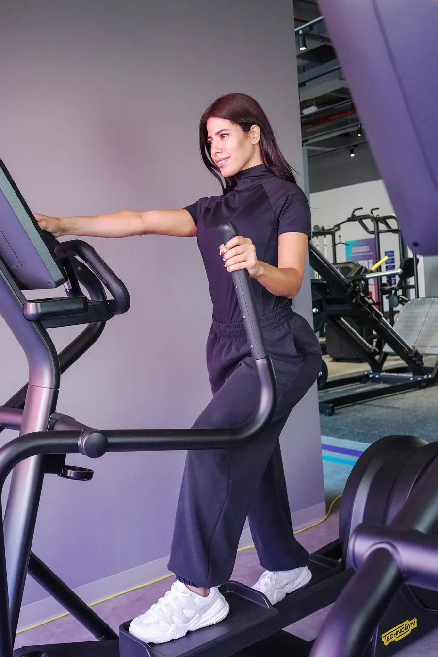 سيدة تتمرن على جهاز الإليبتيكال داخل صالة رياضية حديثة