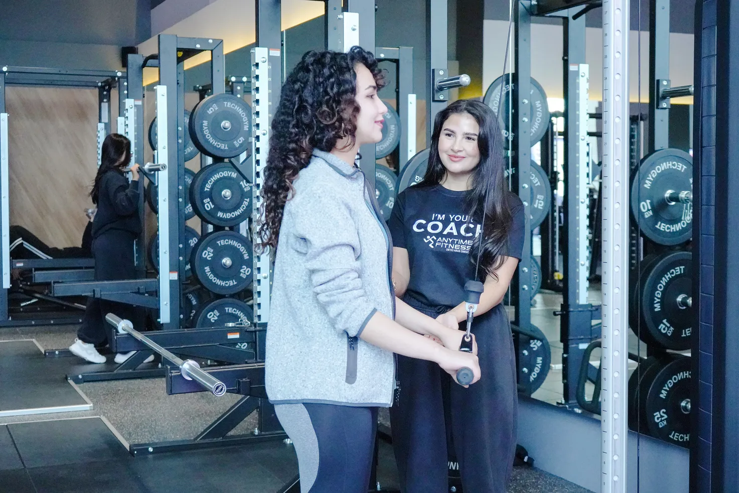 مدربة توجه مشترِكة أثناء استخدام جهاز الكابل في Anytime Fitness