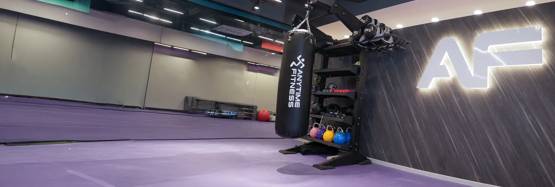 Anytime Fitness functional training area with punching bag, kettlebells, strength equipment, mirrored studio space, and illuminated AF branding.