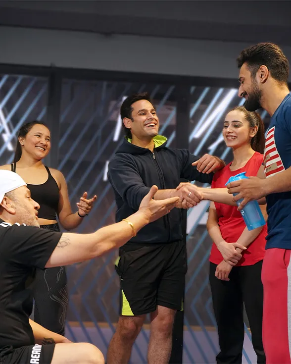 Group of five people in athletic wear smiling and shaking hands in a gym setting.