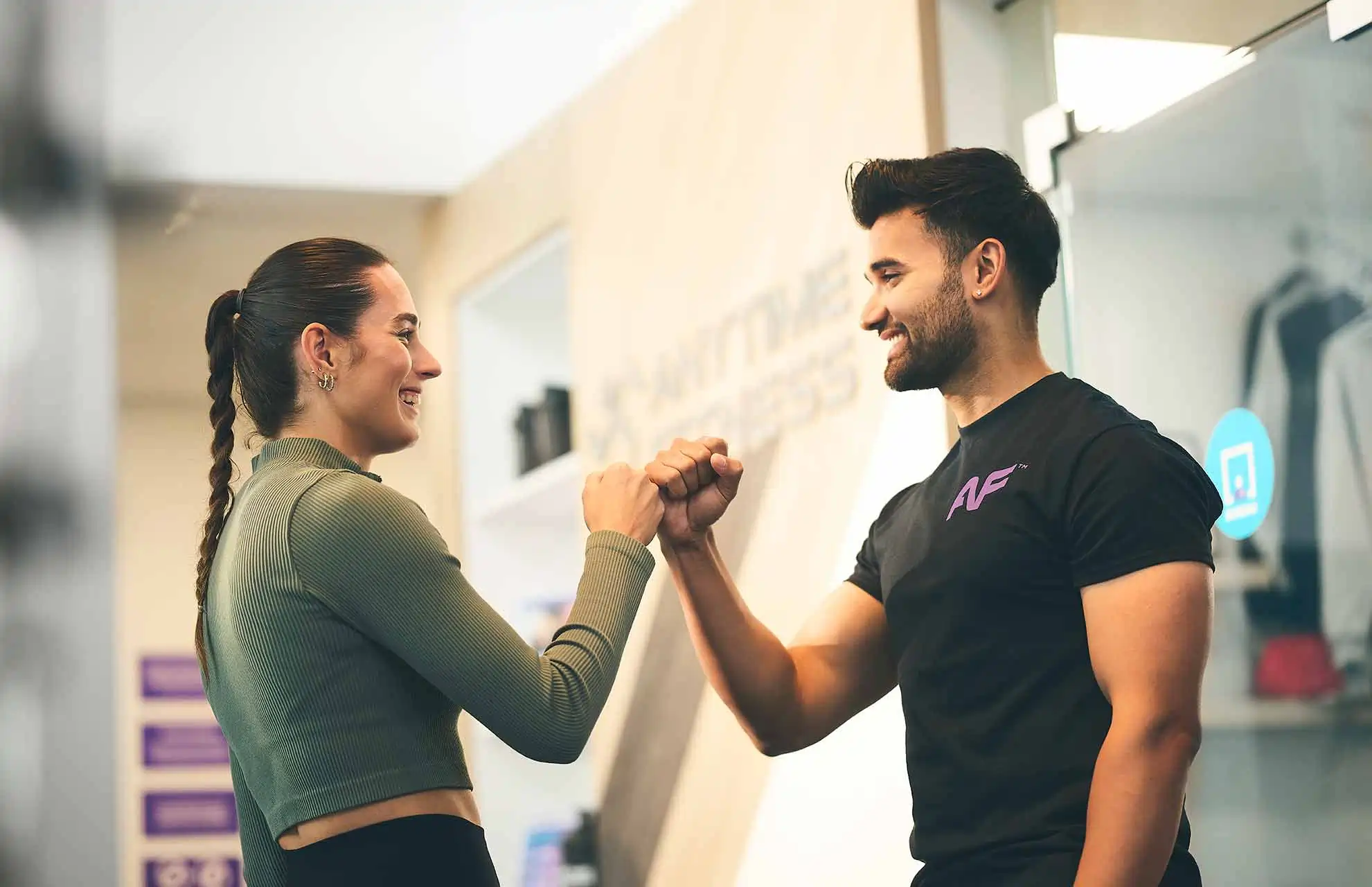 Smiling man and woman fist bumping in a gym setting.