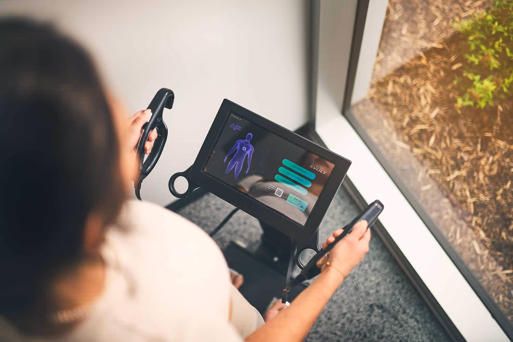 Top view of person holding two handheld devices connected to a screen displaying a human body diagram.