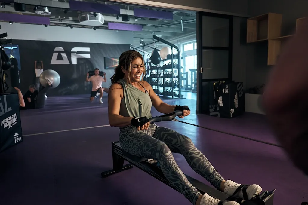 Eine lächelnde Frau in Sportkleidung ruht sich auf einer Trainingsmatte in einem Anytime Fitness Studio aus.
