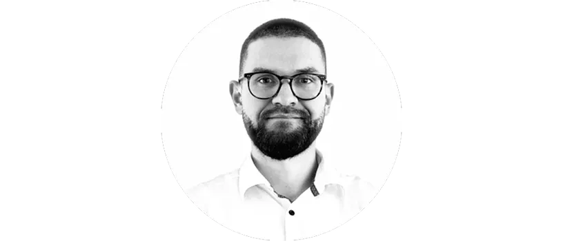 Mann mit kurzem Haar, Bart und Brille, trägt ein weißes Hemd mit Kragen und lächelt leicht.