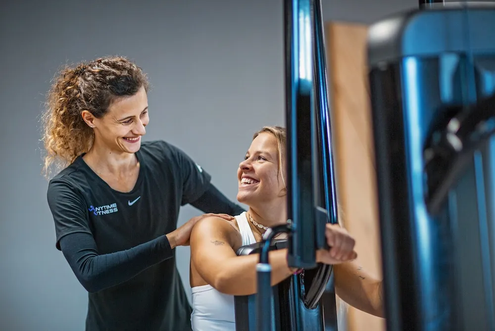 Lächelnde weibliche Trainerin coacht eine Frau an der Kraftmaschine im Fitnessstudio.