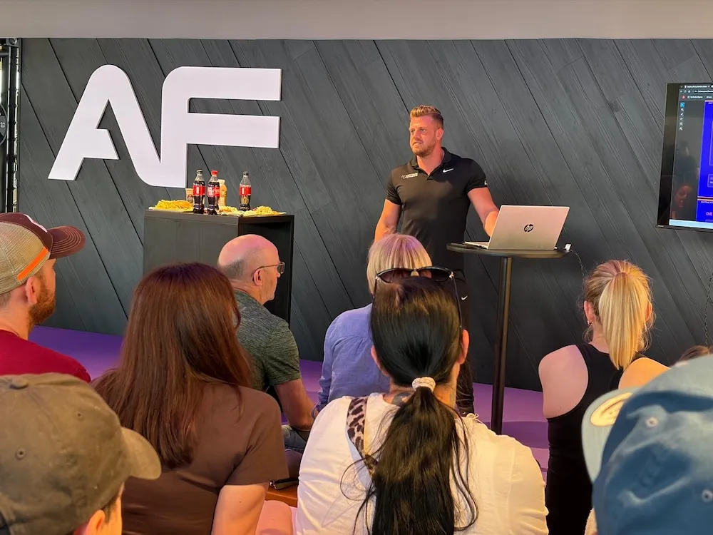 Mann in schwarzem Poloshirt hält vor sitzendem Publikum eine Präsentation vor dem AF-Logo und einem Laptop.