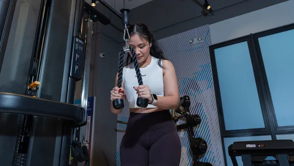 Woman in white top using a cable machine rope attachment for tricep exercise in a gym.