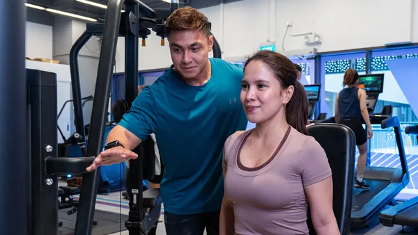 Male trainer guiding woman using gym equipment during workout session.