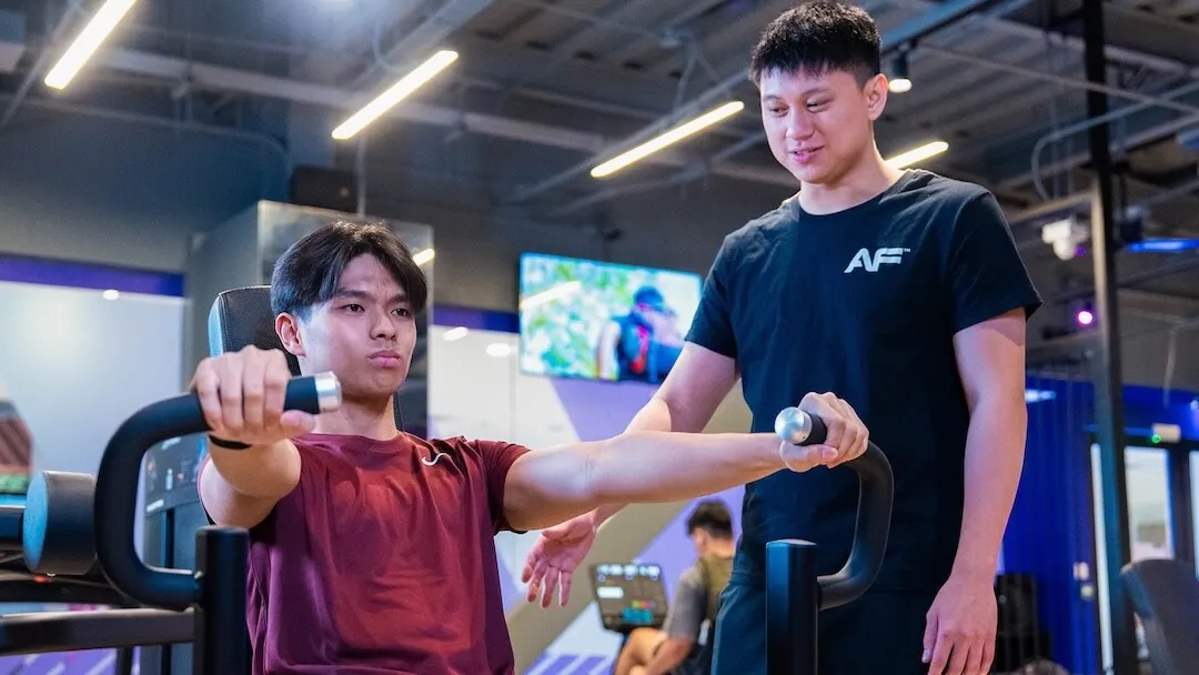 Personal trainer supervising a man using a seated chest machine.