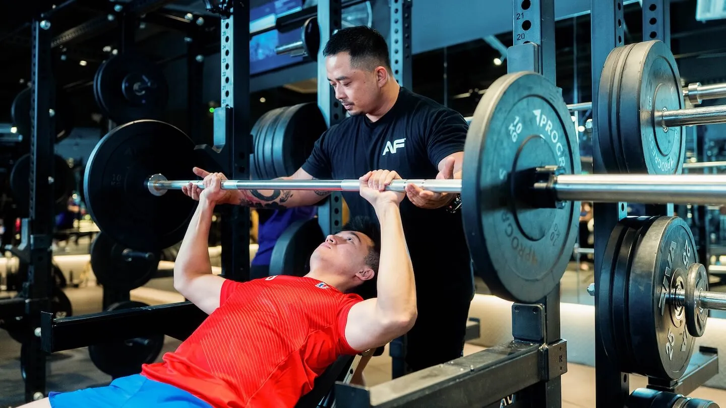 Anytime Fitness personal trainer spotting a male member doing an incline barbell bench press.