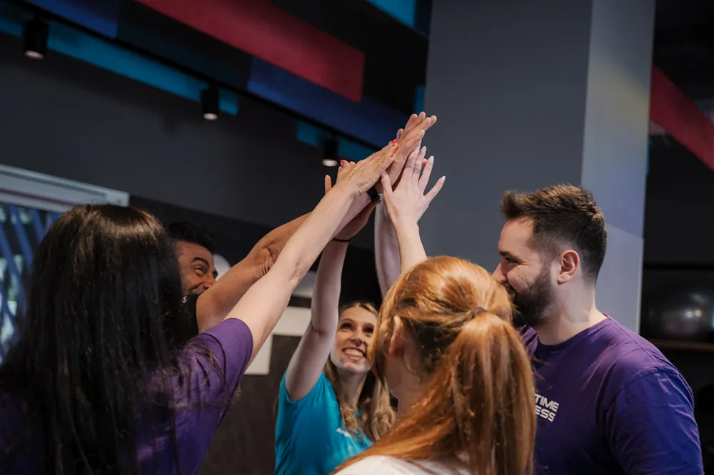 Gruppo di persone in abbigliamento da fitness che danno il cinque a un gruppo in casa con sorrisi.