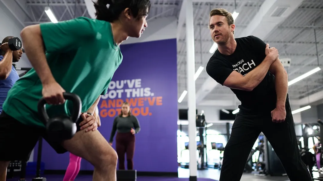 Personal trainer guiding a gym member performing a single-arm kettlebell row.