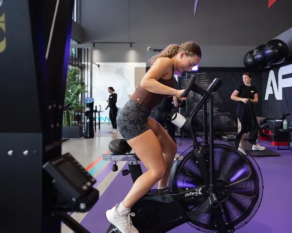 Woman with curly hair cycling intensely on a stationary exercise bike in a gym.
