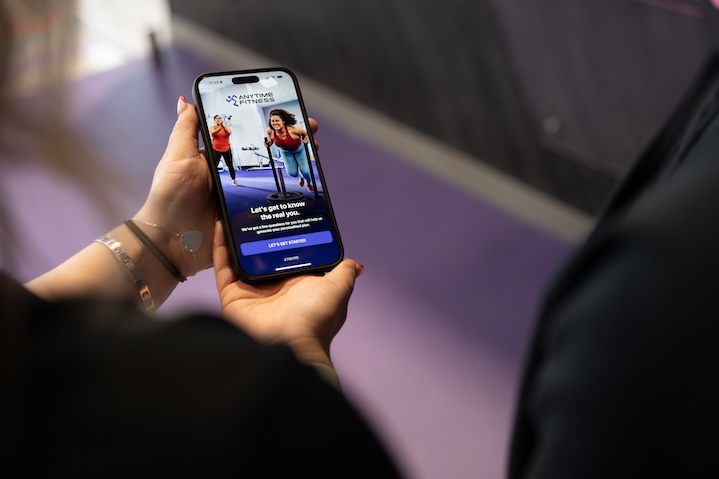 Person holding a phone showing Anytime Fitness app with workout images and a start button.
