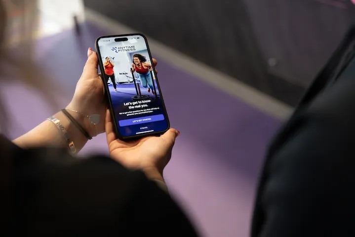 Person holding a phone showing Anytime Fitness app with workout images and a start button.
