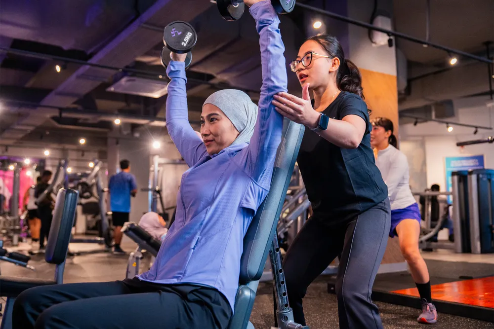 Wanita berhijab dan pakaian olahraga sedang jogging di treadmill di gym modern dengan pemandangan kota.