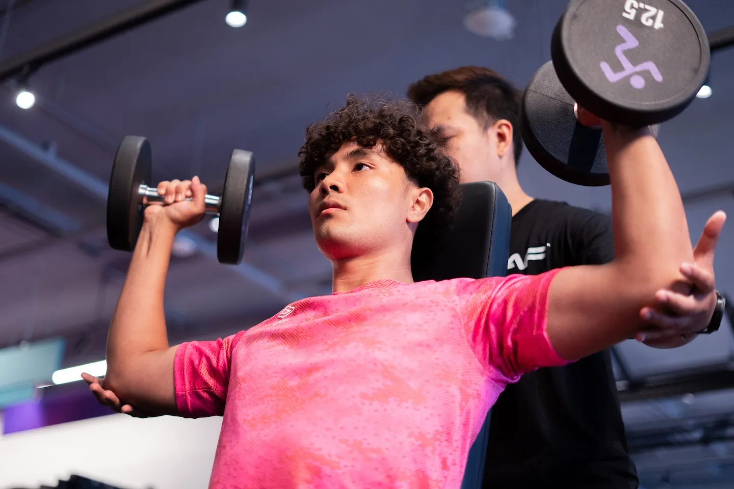 สมาชิกกำลังยกดัมเบลล์โดยมีเทรนเนอร์ Anytime Fitness คอยดูแลอย่างใกล้ชิด