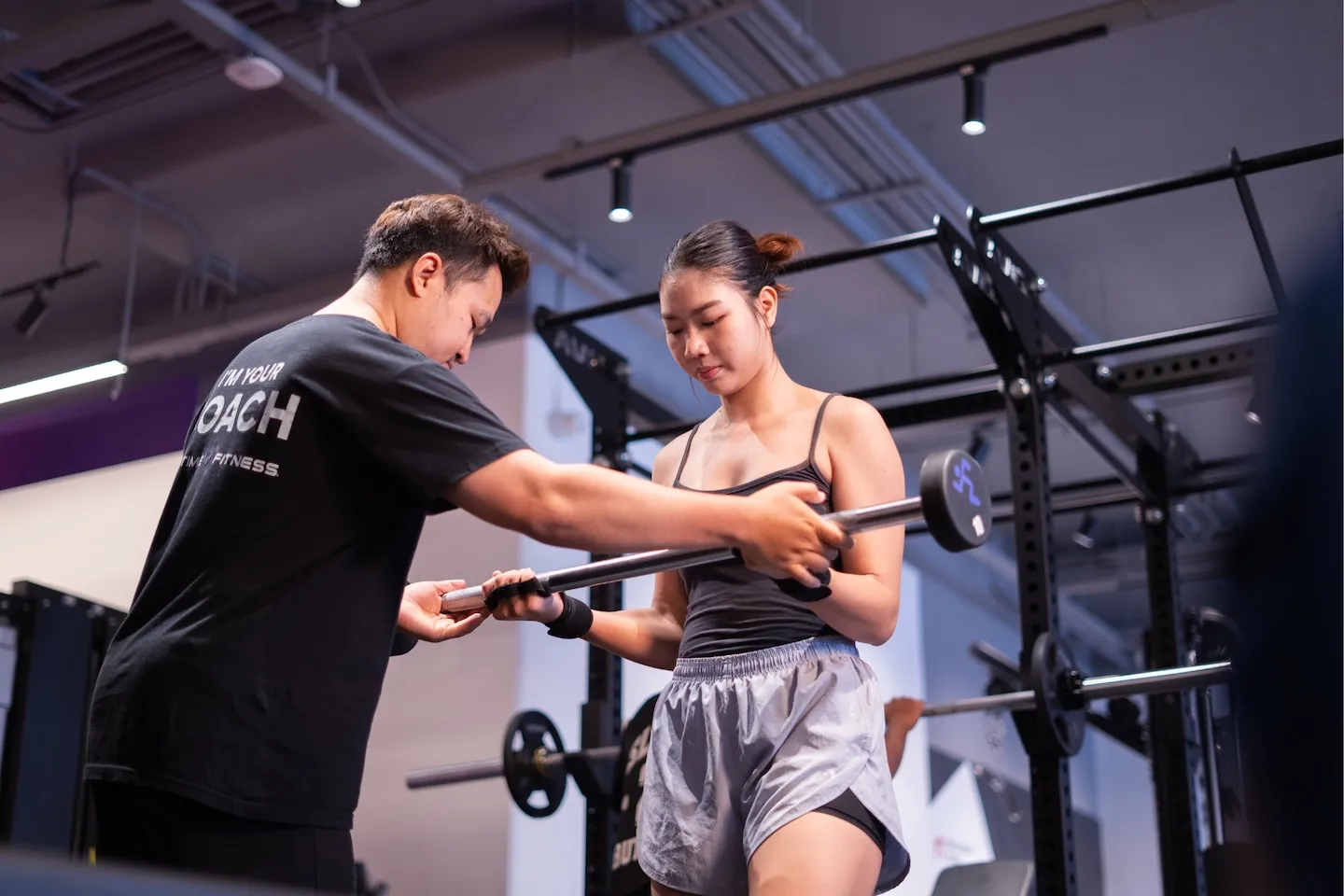 ชายหนุ่มออกกำลังกายท่า Shoulder Press ด้วยดัมเบลล์ โดยมีเทรนเนอร์ส่วนตัว Anytime Fitness คอยจัดท่าและเซฟอย่างปลอดภัย