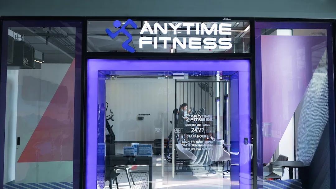 ทางเข้าฟิตเนส Anytime Fitness พร้อมโลโก้แบรนด์และประตูกระจกเปิดบริการ 24 ชั่วโมง