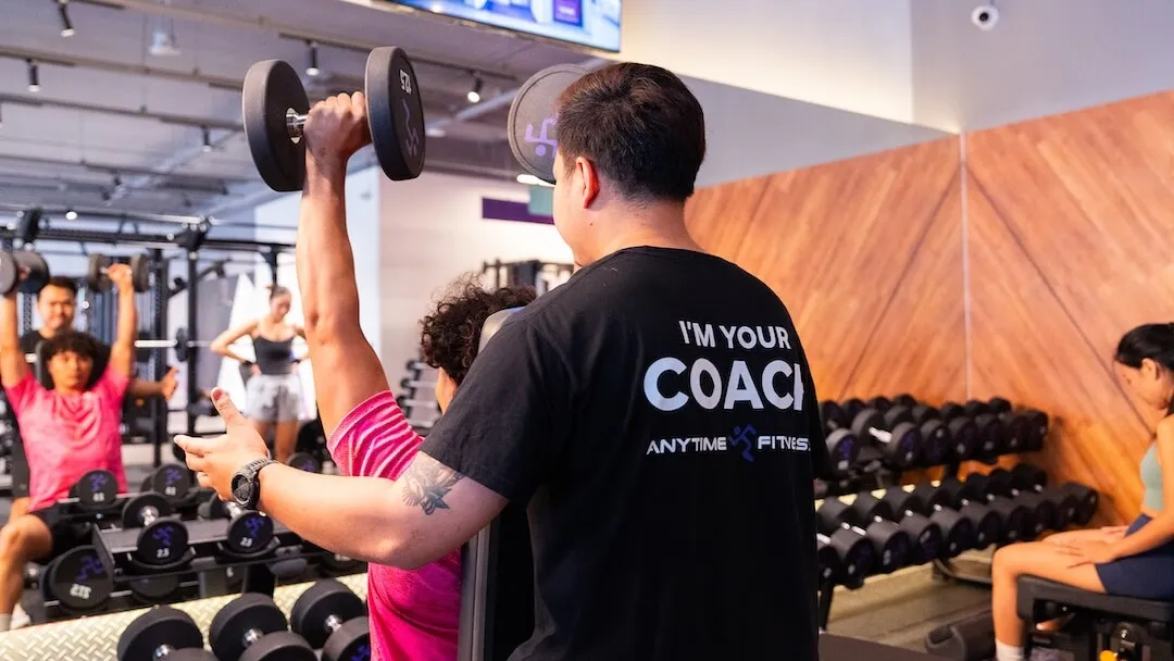 เทรนเนอร์ Anytime Fitness คอยดูแลความปลอดภัยขณะสมาชิกร่ายกายฝึกยกดัมเบล
